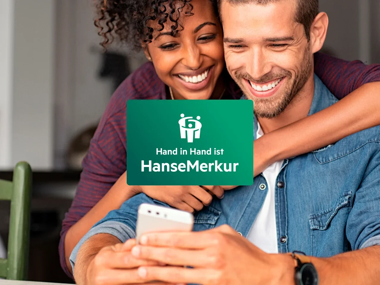 Ein lächelndes Paar schaut auf ein Mobiltelefon. Die Frau umarmt den Mann um die Schultern.