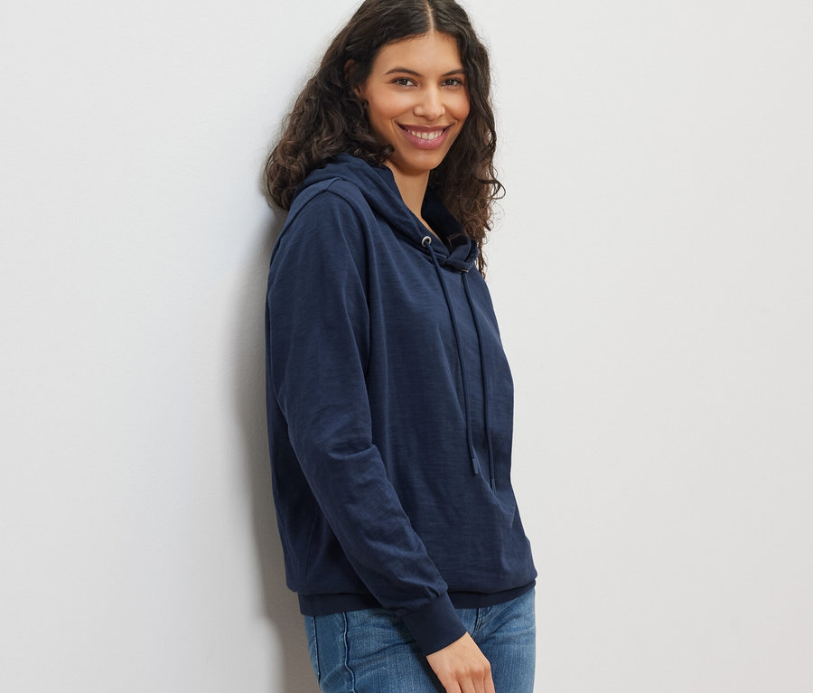 Lächelnde Frau posiert in marineblauem Jersey-Hoodie und Jeans.