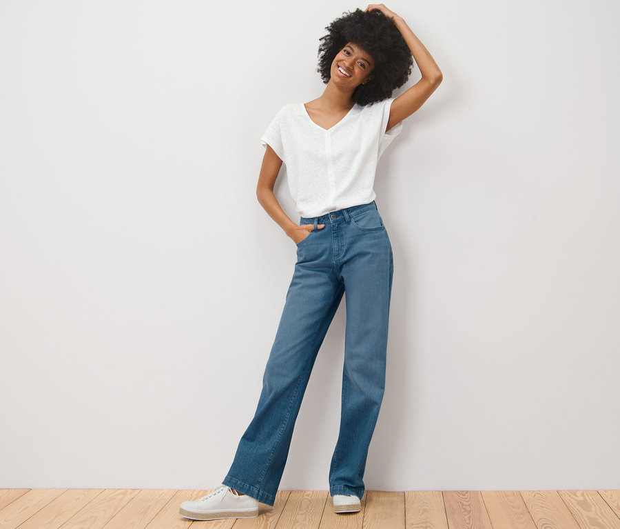 Eine Frau mit Afro posiert in einer »Neni« Palazzo Jeans und einem weißen T-Shirt an einer weißen Wand.