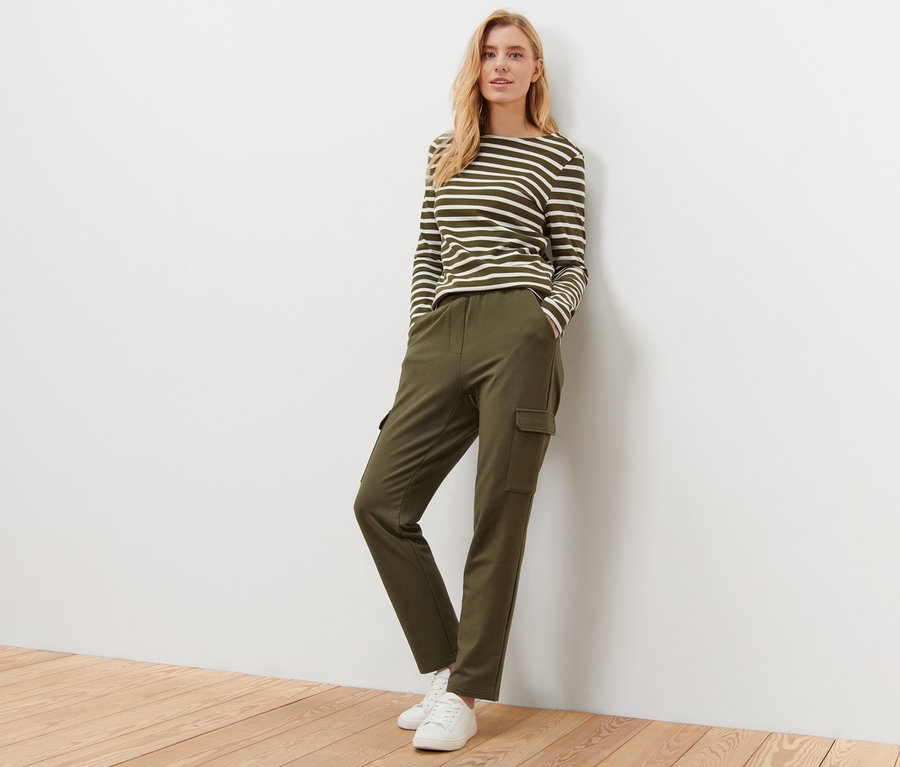 Blonde Frau steht an einer Wand und trägt eine khaki Joggpants mit Cargo-Taschen.