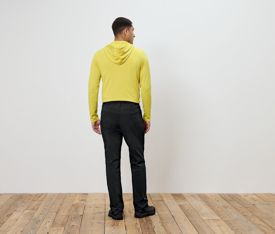 Mann in gelbem Kapuzenpullover und schwarzen Hosen steht mit dem Rücken zur Kamera.