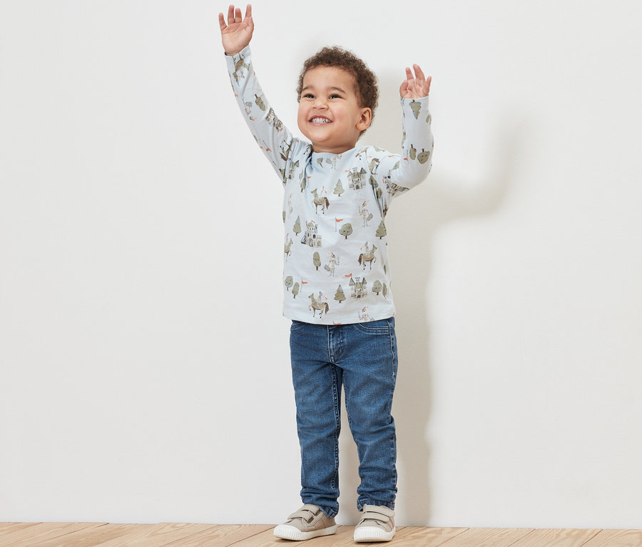 Junge mit erhobenen Armen trägt Kinder-Jeans – Fit »Jonas« und ein bedrucktes Shirt.