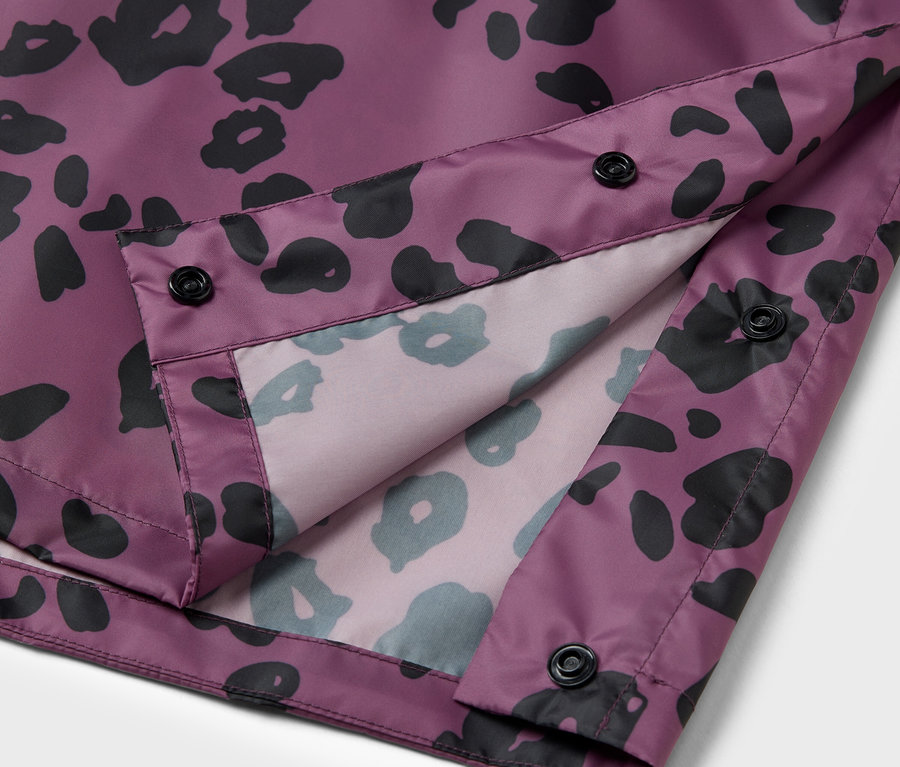 Detail einer lila Jacke mit schwarzem Tiermuster und schwarzen Knöpfen.