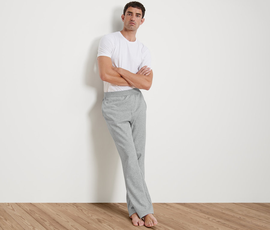 Mann lehnt an Wand, trägt weißes T-Shirt und Homewearhose.