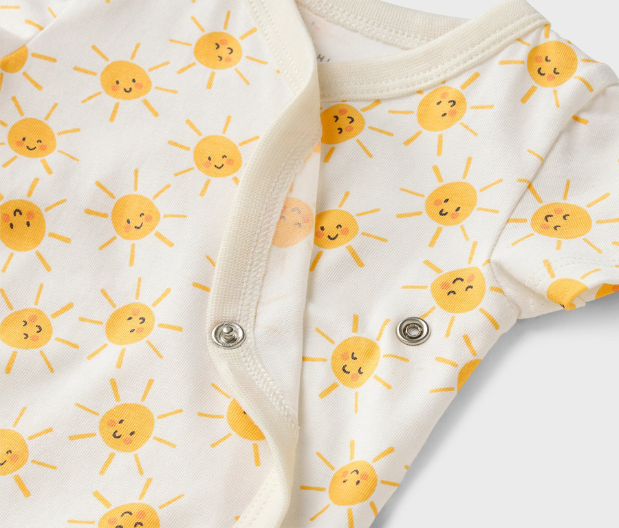 Nahaufnahme eines weißen Baby-Bodys mit gelbem Sonnenmuster und Druckknöpfen.
