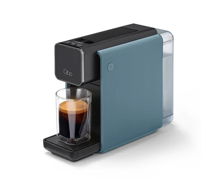 Eine "Qbo ONE" Kapselmaschine in Misty Blue und Schwarz mit einer Tasse Espresso auf der Abtropfschale.