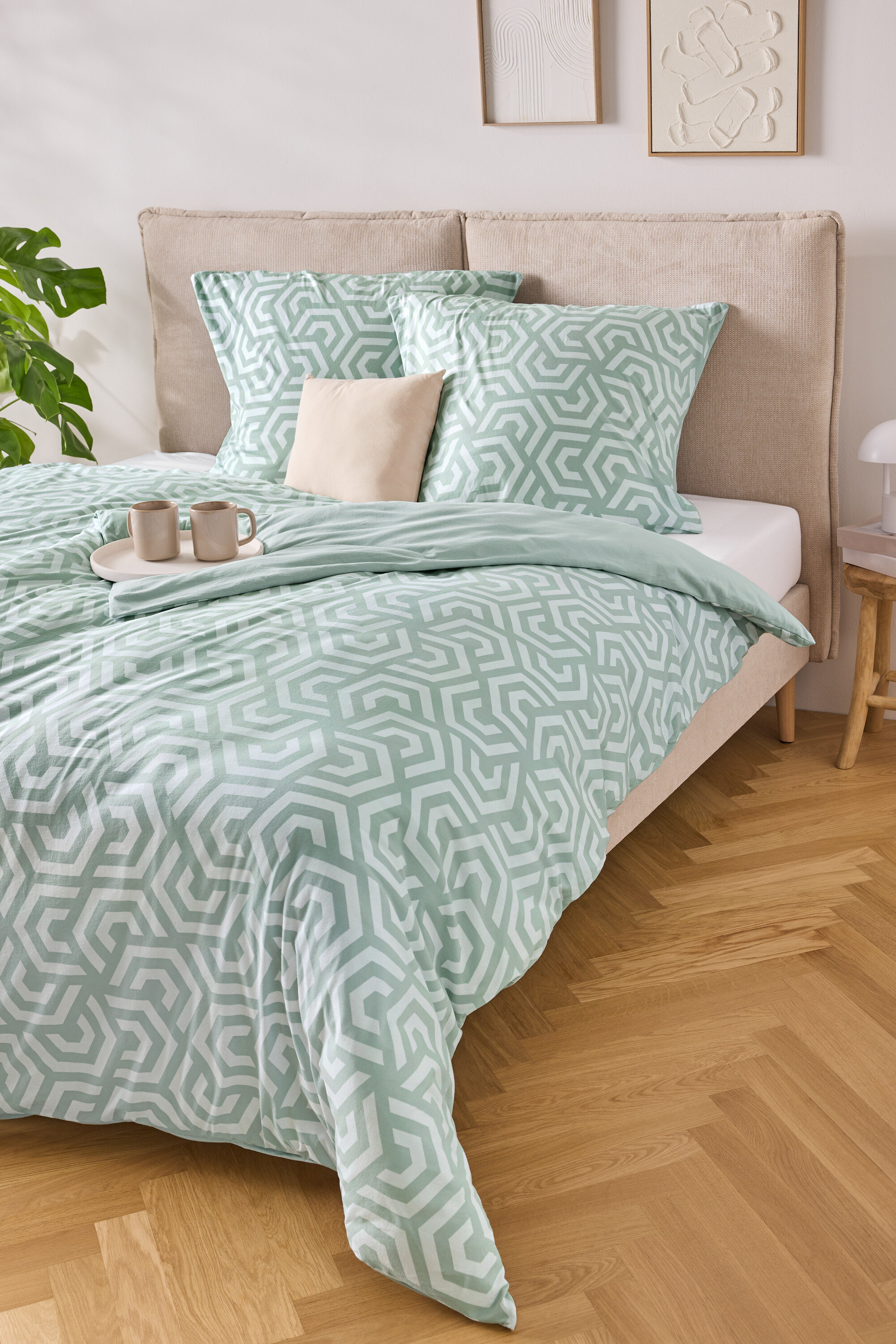 Ein Bett mit hellblau-weiß gestreifter Bettwäsche, zwei Kissen und einer Ablage mit zwei Tassen darauf.