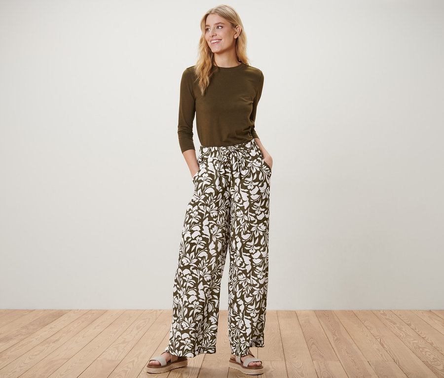 Frau posiert stehend in bedruckter Schlupfhose, olivgrünem Oberteil und Sandalen.