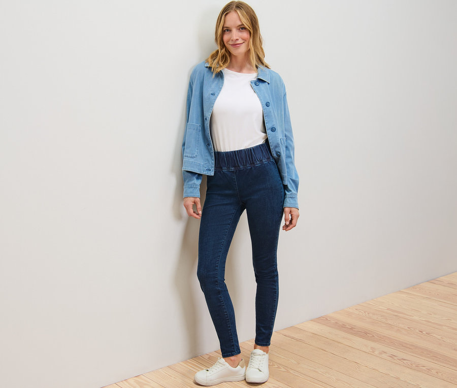 Frau posiert in High-Waist-Denim-Leggings, einem weißen T-Shirt und einer blauen Jacke.