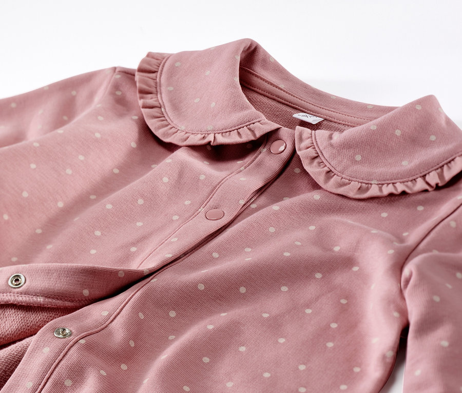 Detailansicht einer rosa Kinder-Sweatjacke mit Volant und weißen Punkten.
