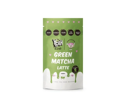 Grün-weisser Beutel von The Yeah Blend Green Matcha Latte, 100 g. Der grüne obere Teil zeigt das Logo "The Yeah Blend" und eine "Baristacoin"-Figur. "Green Matcha Latte" steht in Grün geschrieben, mit einem wellenförmigen weissen unteren Bereich, auf dem "I LOVE YOU SOOO MATCHA" steht. Etiketten weisen auf "VEGAN", "NATÜRLICH", "OHNE PALMÖL", "OHNE FARBSTOFFE", "OHNE EMULGATOREN" hin.