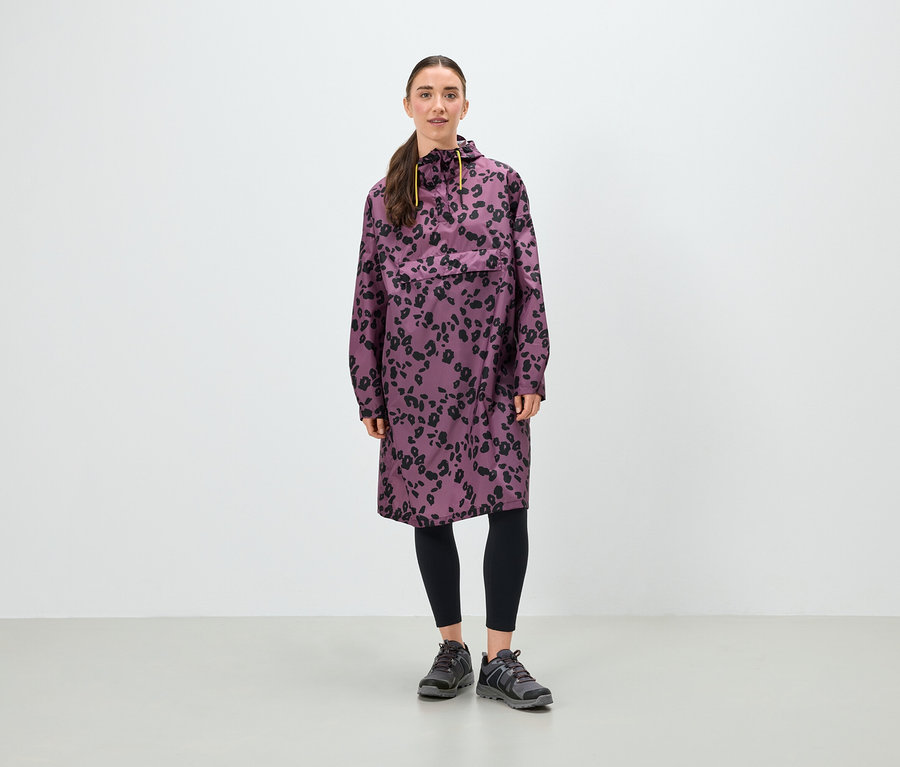 Frau steht und trägt eine lila Tunika mit schwarzem Blumenmuster, schwarze Leggings und graue Schuhe.