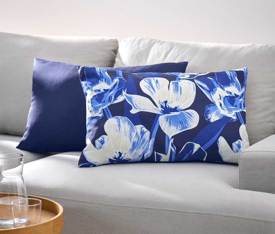 Auf einem hellgrauen Sofa liegen zwei Dekokissen-Bezüge, einer ist dunkelblau, der andere hat ein Blumenmuster.