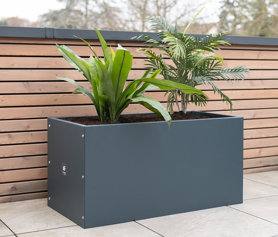 Ein anthrazitfarbener Herstera Garden Pflanzkasten mit Pflanzen auf einer Terrasse.