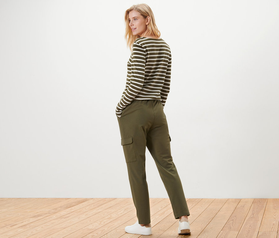 Frau posiert in Khaki-Joggpants mit Cargo-Taschen und einem gestreiften Oberteil.