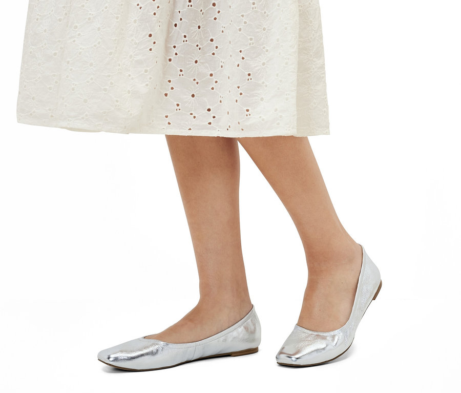 Beine einer Frau in einem weißen Kleid und Leder-Ballerinas.